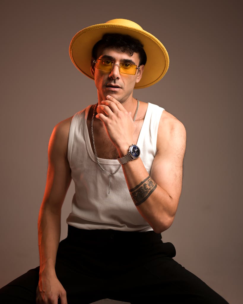 A man in a yellow hat and sunglasses sitting on a stool