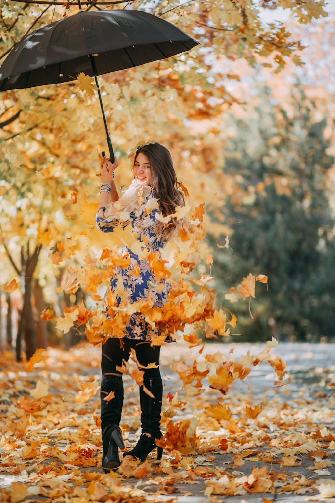Smiling woman holding an umbrella surrounded by vibrant autumn leaves in a park.