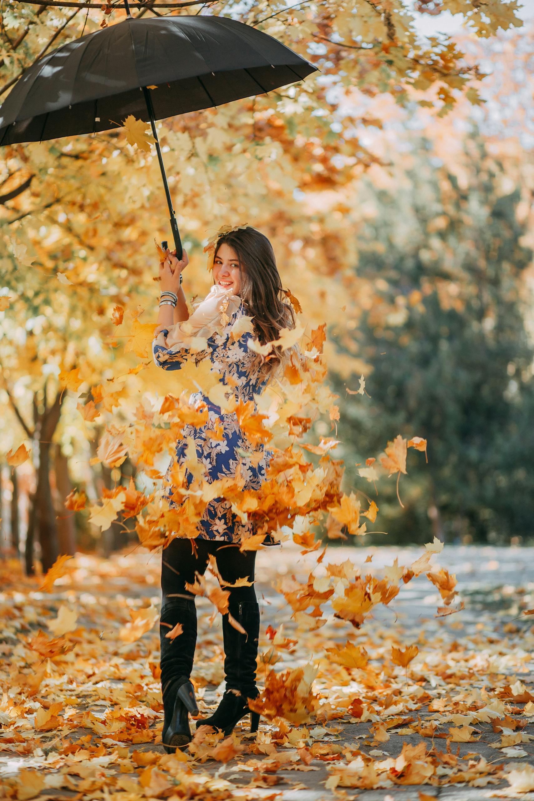 Smiling woman holding an umbrella surrounded by vibrant autumn leaves in a park.